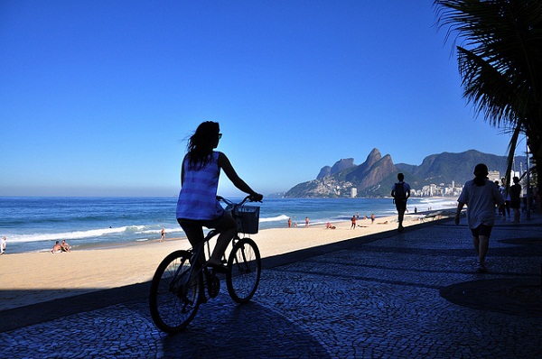 Foto mostra mulher andando de bicicleta na orla do Rio