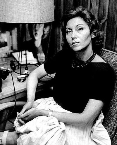 Clarice Lispector em sua casa, no Leme, vestindo uma blusa preta e uma saia clara, olhando para o fotógrafo