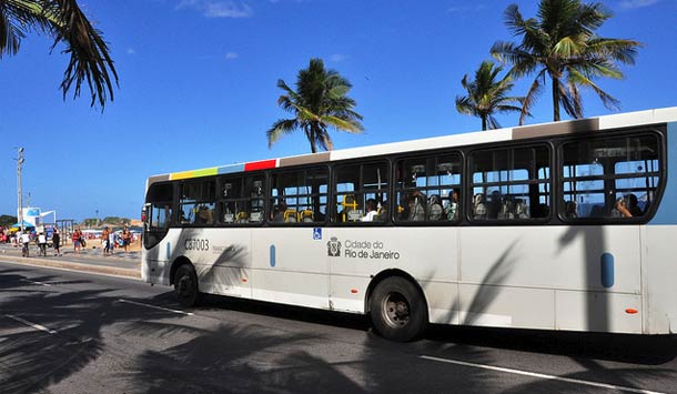 Ônibus em pista na rua com céu azul e palmeiras ao fundo