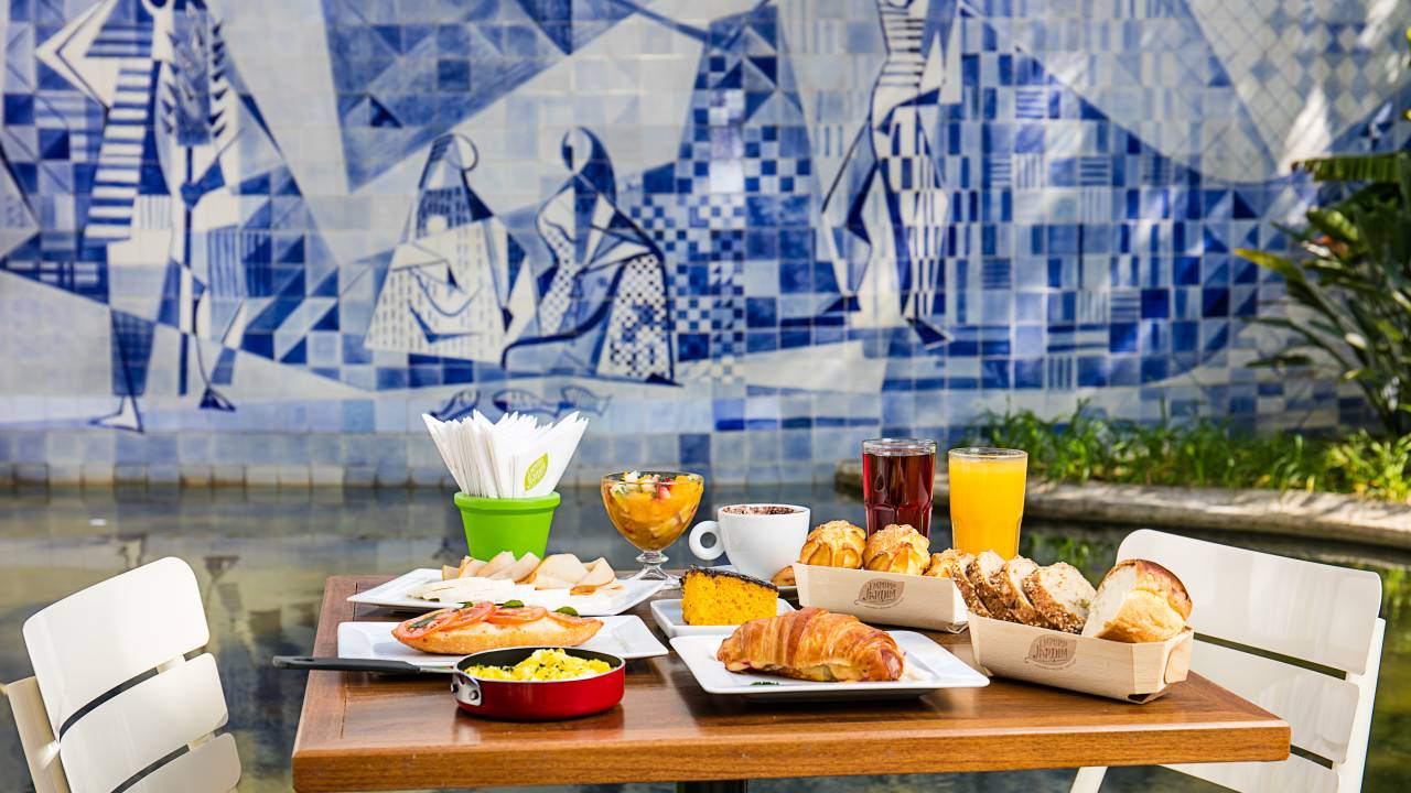 mesa de café da manhã posta em frente ao laguinho do Instituto Moreira Salles, com a parede de azulejos pintados
