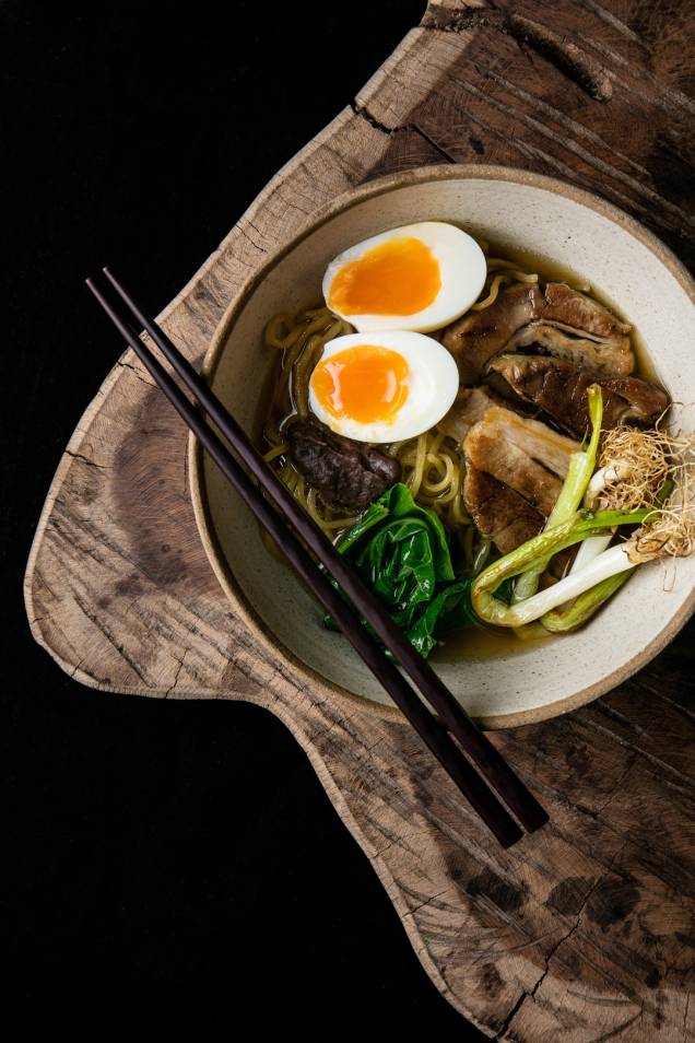 O "nosso rámen" caldo de porco, macarrão, couve seca, ovo, cebolinha tostada, pasta de feijão preto e barriga suína