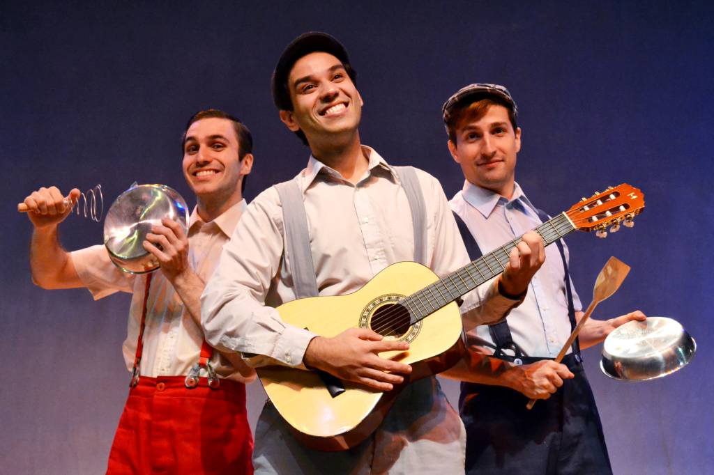 Tres atores no palco, com roupas de época e instrumentos musicais