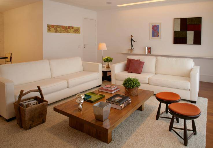 Banquinhos mocho do designer brasileiro S&eacute;rgio Rodrigues, tapete grande, tecidos coloridos, arranjo de flores naturais e quadro Concei&ccedil;&atilde;o Rodrigues, da galeria HAP, comp&otilde;em esta aconchegante sala de estar.<br>