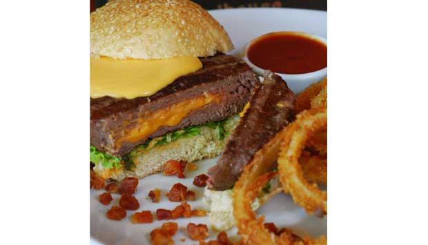 (R$ 31,90) Indicamos esse suculento hambúrguer (200 gramas) de carne bovina recheado de cheddar e coberto de molho do mesmo queijo e bacon, servido com alface, tomate e cebola no pão com gergelim<br>