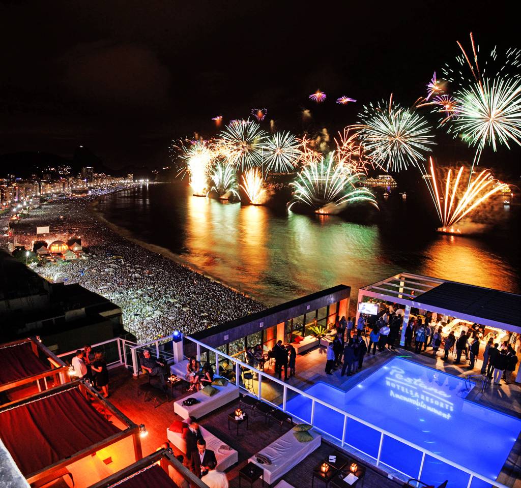 Orla de Copacabana no dia do ano novo com fogos de artifício no céu com o mar a frente.