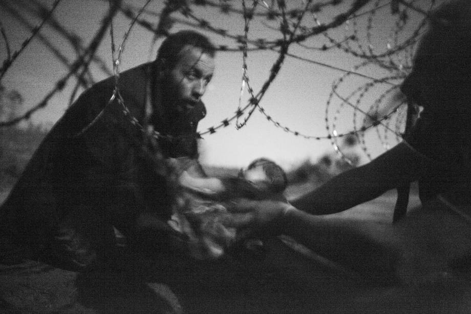 Warren Richardson: Hope for a New Life mostra um bebê sendo passado pelo pai refugiado para o outro lado da frointeira