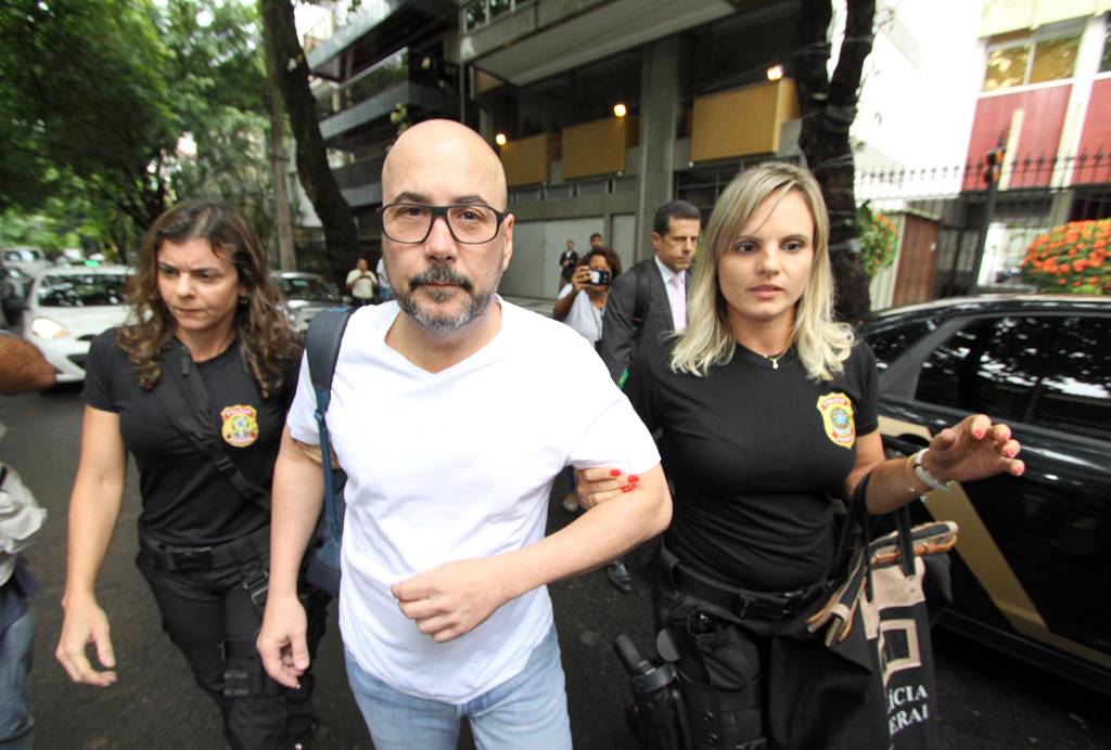 A imagem mostra o presidente da Fecomercio, Orlando DIniz, escoltado por duas policiais federais, ao ser preso