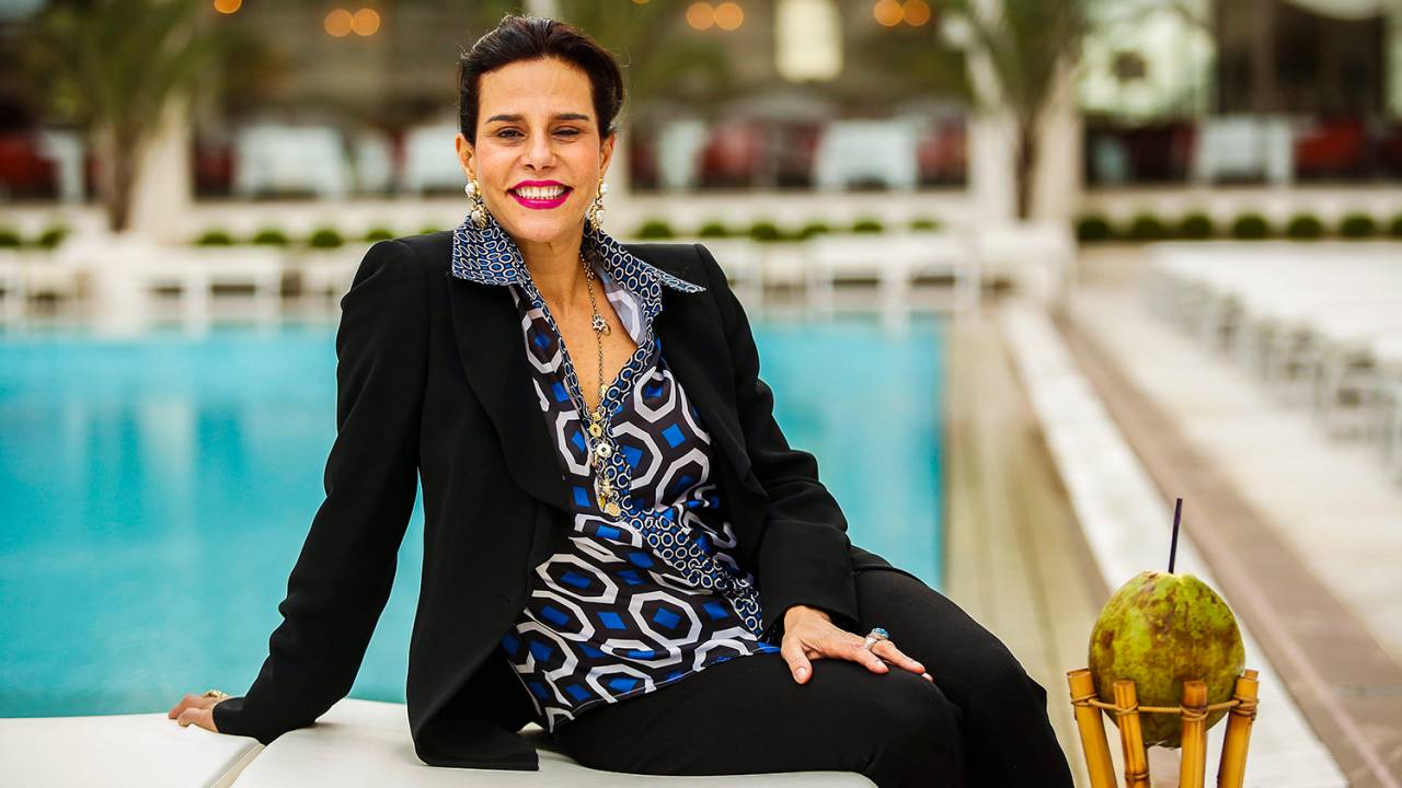 Narcisa Tamborindeguy - youtube sentada à beira da piscina, de terno preto e camisa azul estampada.