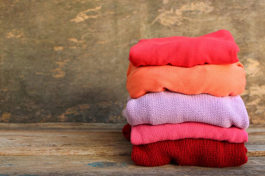 Pilha de roupas de lã com tons de laranja, rosa, roxo