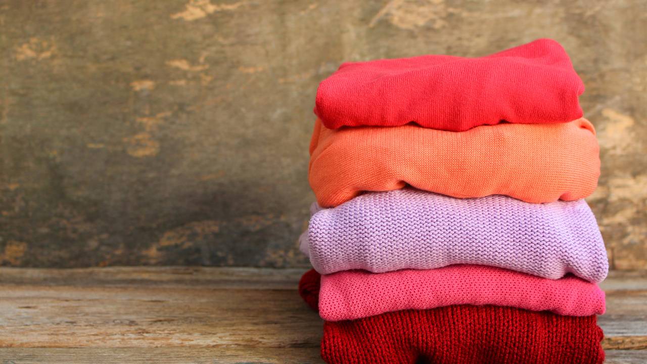 Pilha de roupas de lã com tons de laranja, rosa, roxo