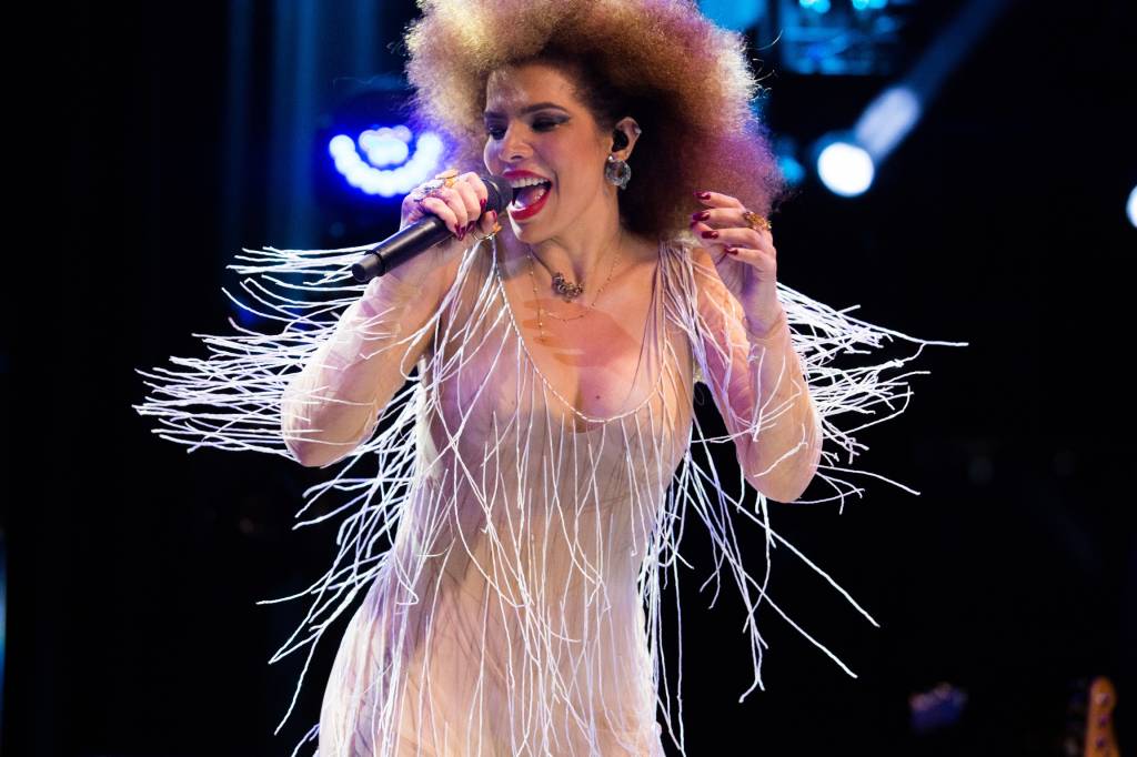 A cantora Vanessa da Mata no palco, segurando um microfone, em movimento