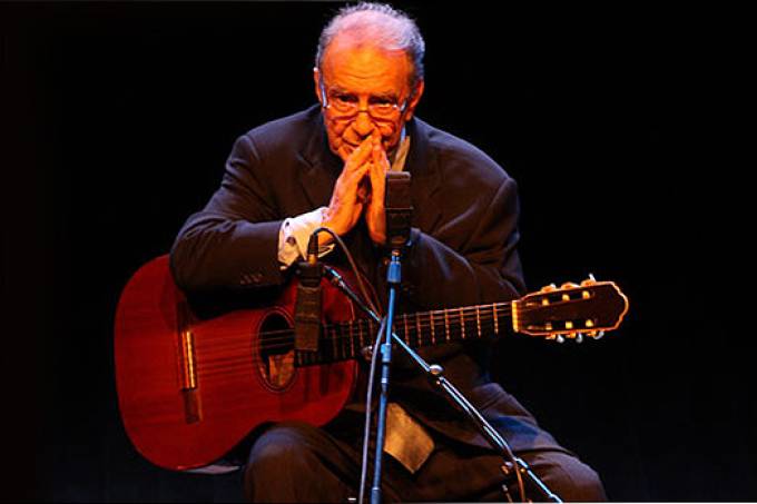 A imagem mostra João Gilberto, no banquinho, com o violão