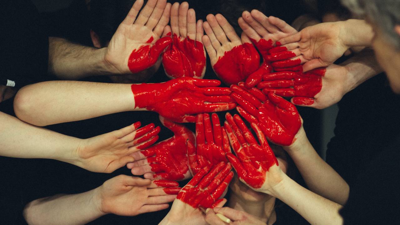 Várias mãos pintadas de vermelho formando um coração