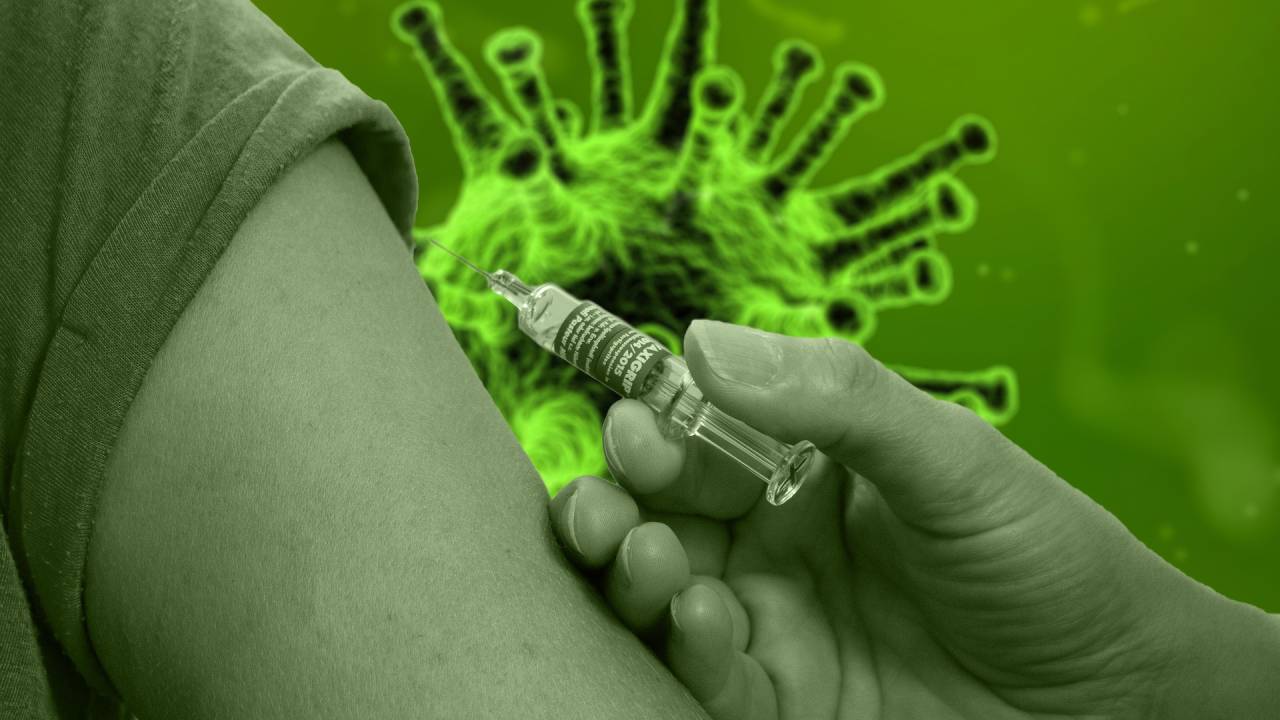A imagem mostra um braço prestes a ser vacinado, e a ilustração do vírus ao fundo