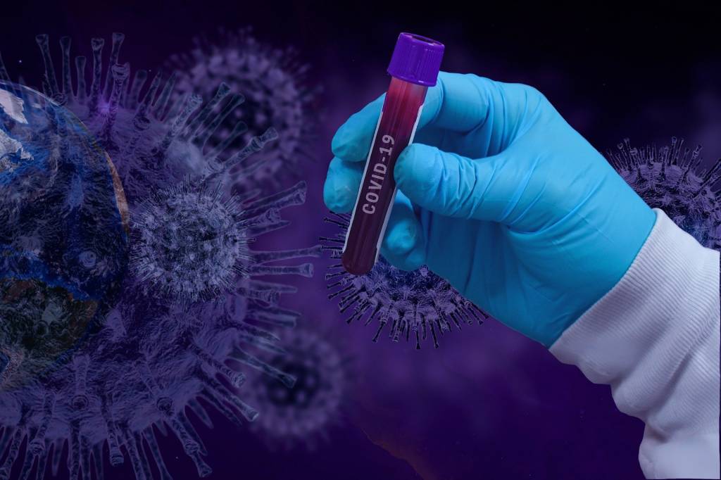 Imagem mostra amostra de sangue em frente à imagem que representa o vírus SARS-CoV-2