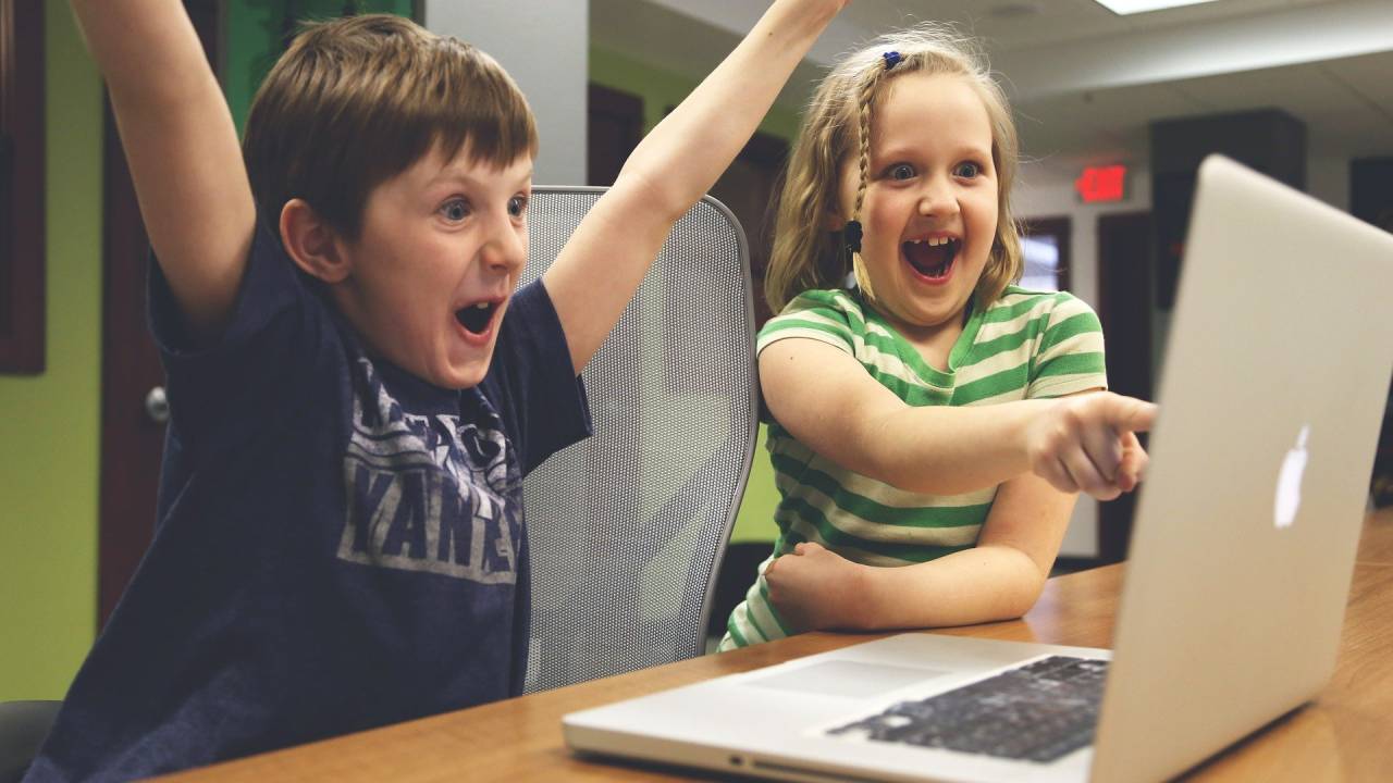 Menino e menina vibrando em frente ao computador