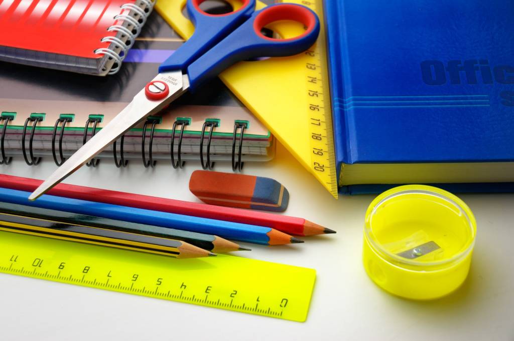 mesa com materiais escolares espalhados, como tesoura, lápis, borrancha, caderno e régua