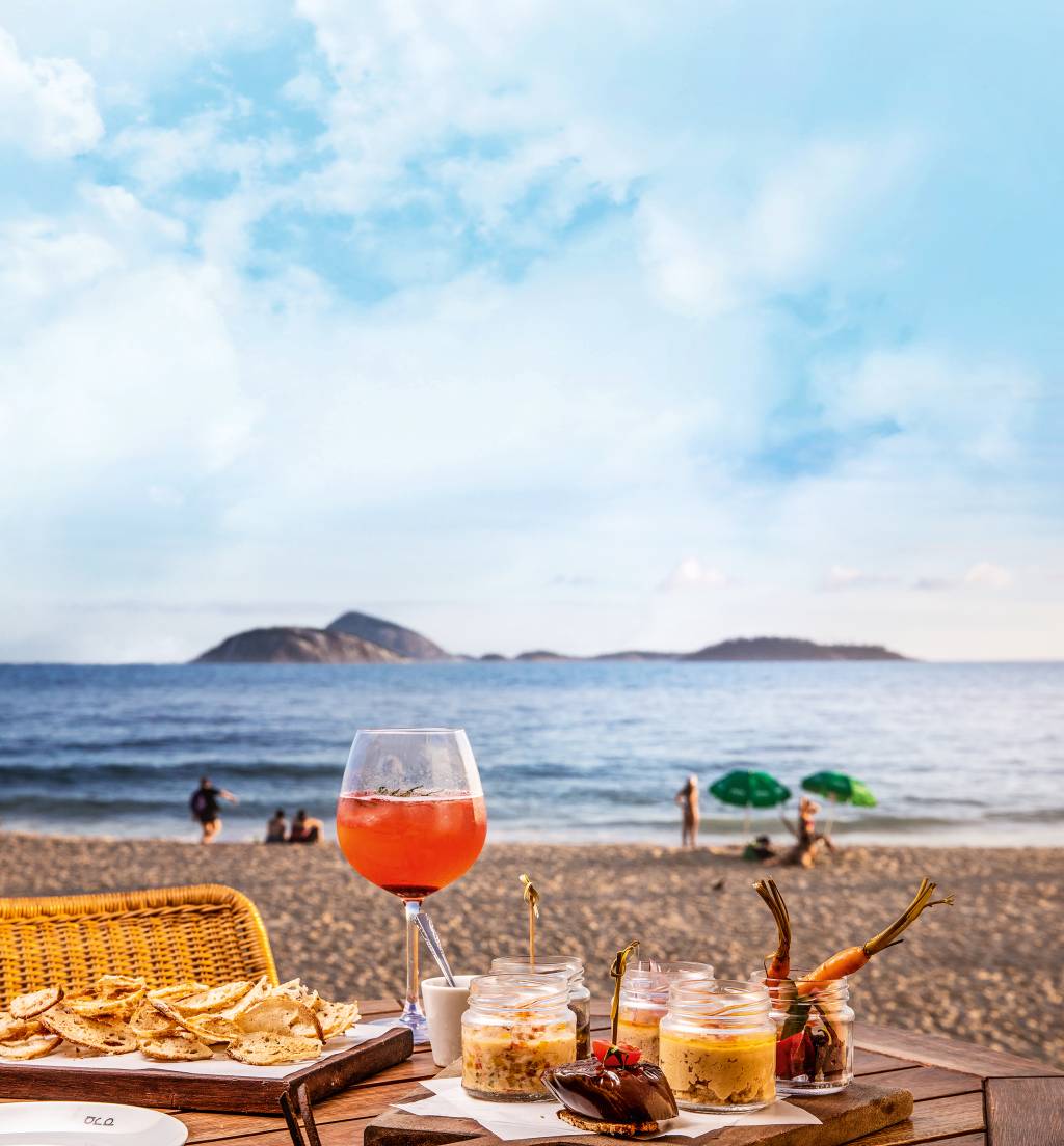 Mesa posta com petiscos e drinque em frente à praia do Arpoador