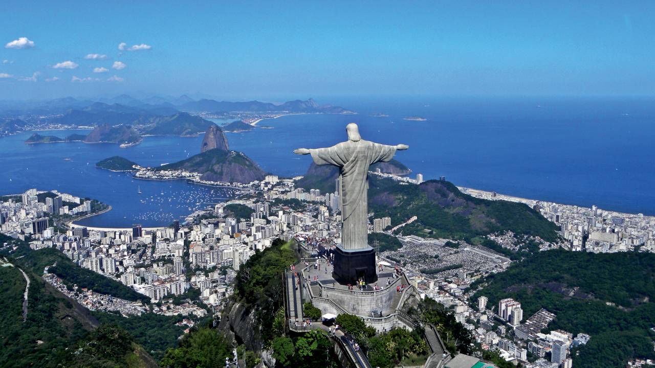 A imagem mostra a estátua do Cristo Redentor com o mar e a cidade do Rio embaixo