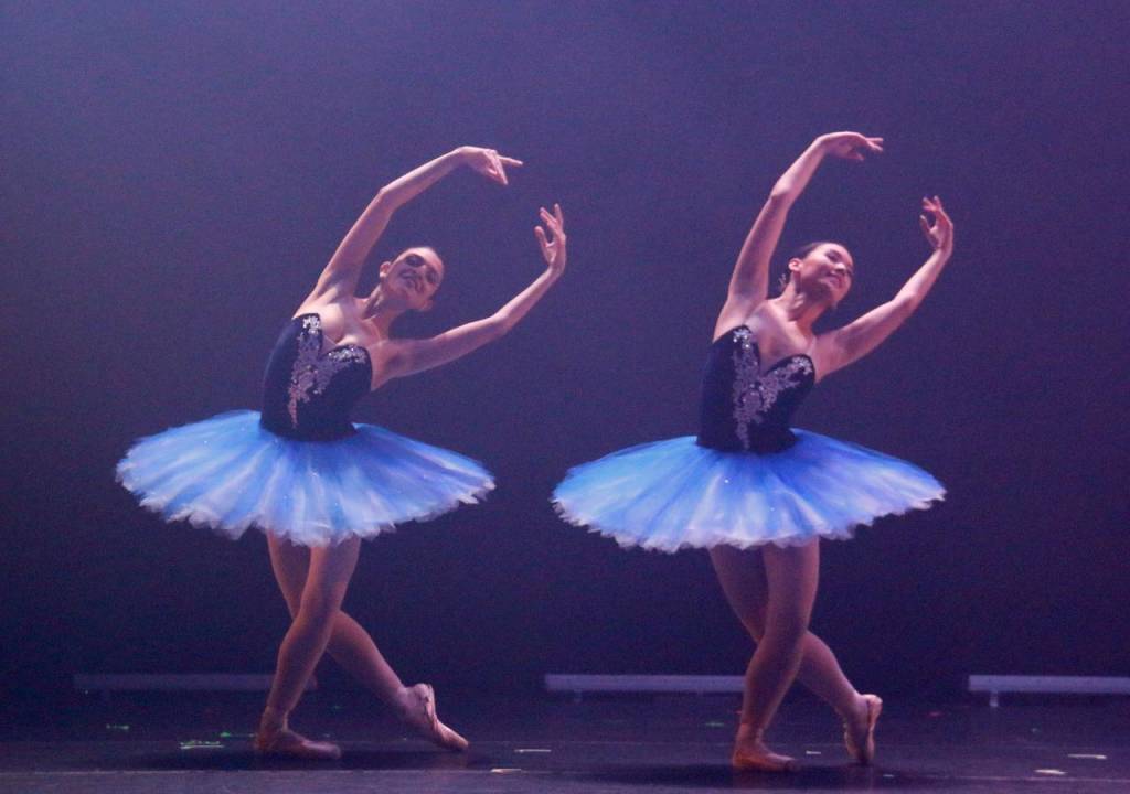 Duas bailarinas no palco, fazendo passos de balé, inclinadas para a esquerda