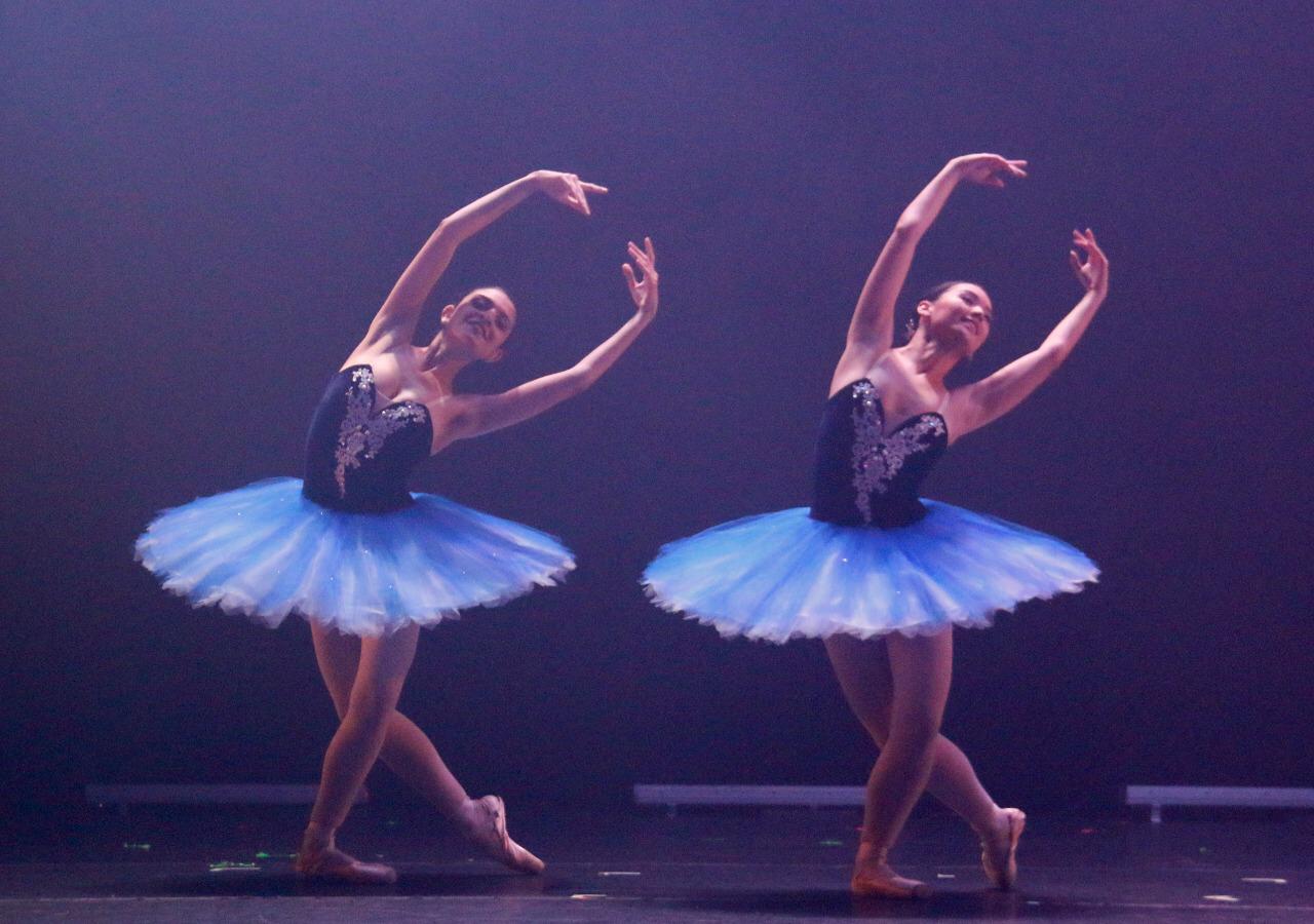 Cia Jovem de Ballet Rio de Janeiro ft Divulgação Duas bailarinas no palco, fazendo passos de balé, inclinadas para a esquerda