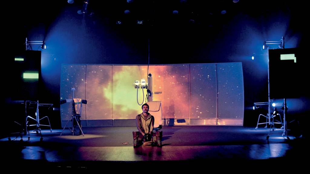 O ator Eriberto Leão no palco da peça O Astronauta, com um telão ao fundo que simula o espaço sideral