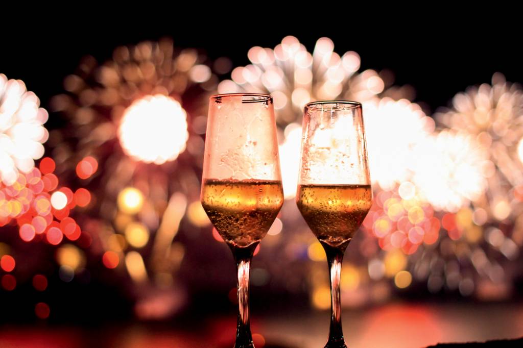 Duas taças de champanhe com fogos de artifício ao fundo