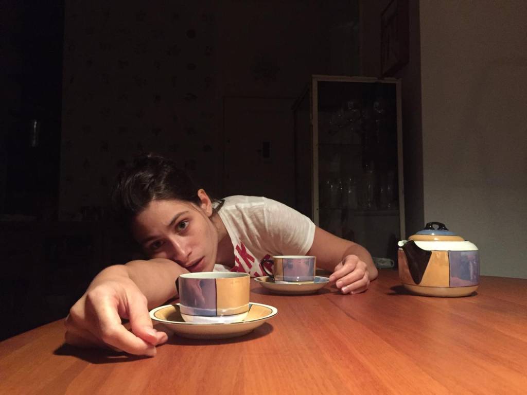 Luisa Arraes debruçda sobre a mesa, com xícaras de café ao lado