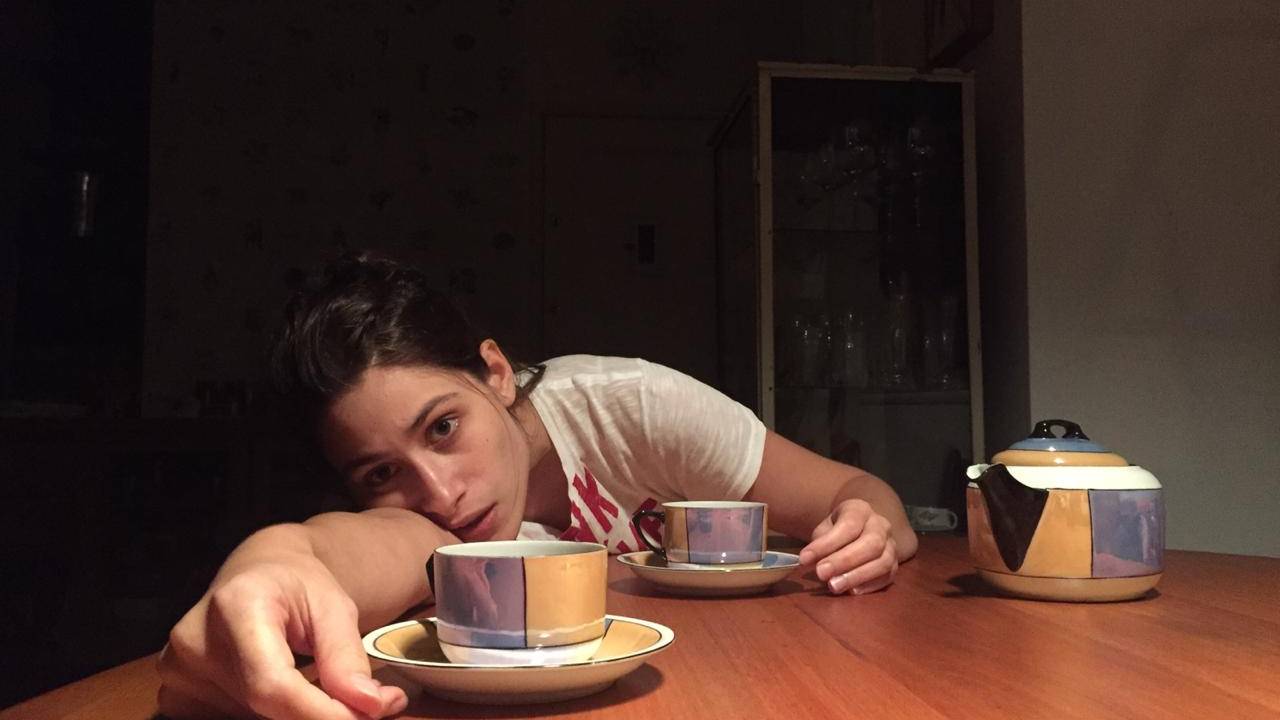 Luisa Arraes debruçda sobre a mesa, com xícaras de café ao lado