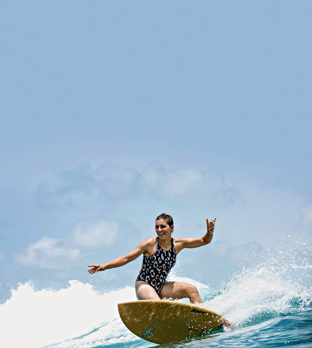 A imagem mostra a surfista Maya Gabeira fazendo uma manobra em uma onda no mar das Ilhas Maldivas
