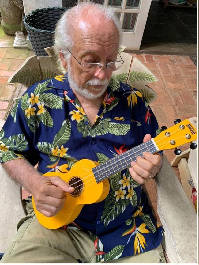 Homem idoso vestido uma camisa florida e tocando violão