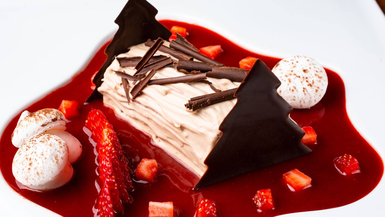 A imagem mostra um bûche de Noel, sobremesa com calda de morango e chocolate