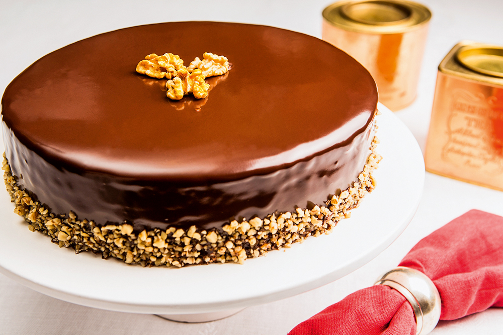 A imagem mostra uma torta de nozes coberta de calda de chocolate