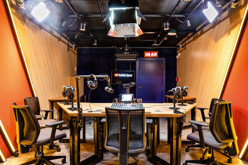 Estúdio de rádio no Youtube Space, com uma mesa ao centro, com vários microfones, cadeiras e refletores presos ao teto