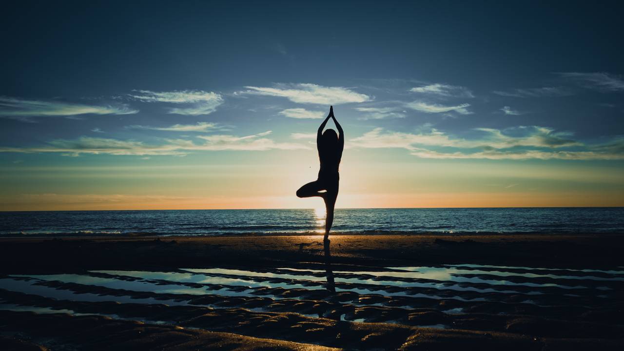 Pessoa em posição de ioga na praia ao nascer do sol.
