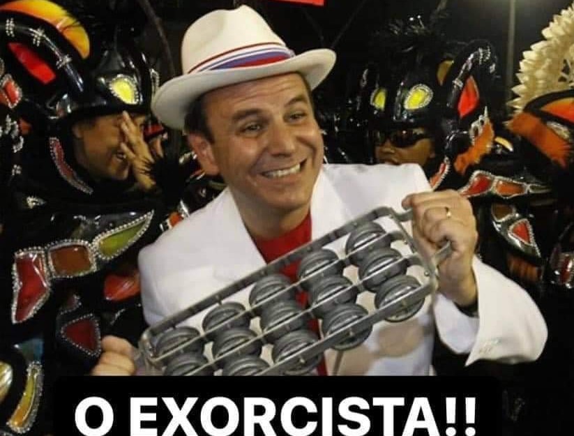 A imagem mostra o prefeito eleito do Rio, Eduardo Paes, de chapéu e terno brancos, entre os ritmistas de uma escola de samba
