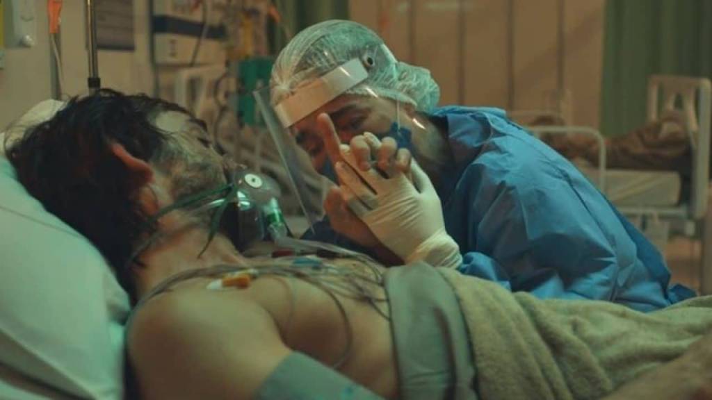 Personagens de Julio Andrade e Marjorie Estiano se abraçam. Ele está de máscara de oxigênio, num leito de UTI