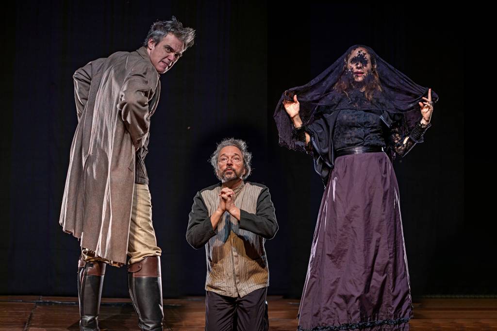 Três atores no palco, com roupas de época