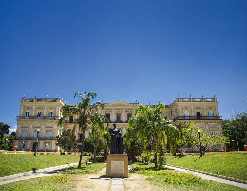 A imagem mostra a fachada do Museu Nacional em meio a um jardim