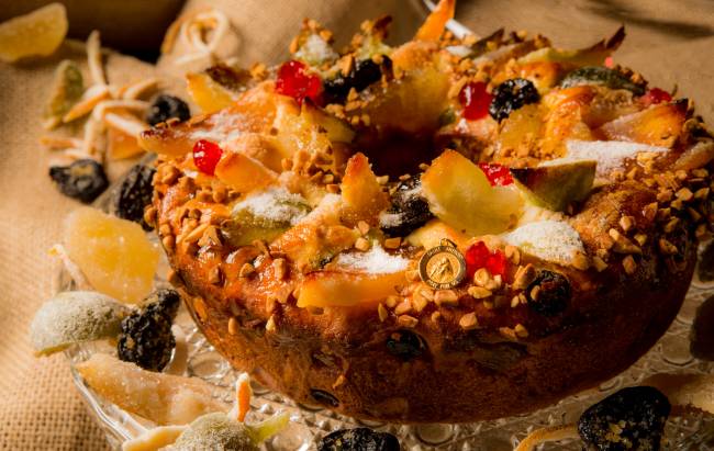 A imagem mostra uma rosca de reis, pão doce redondo coberto de frutas cristalizadas