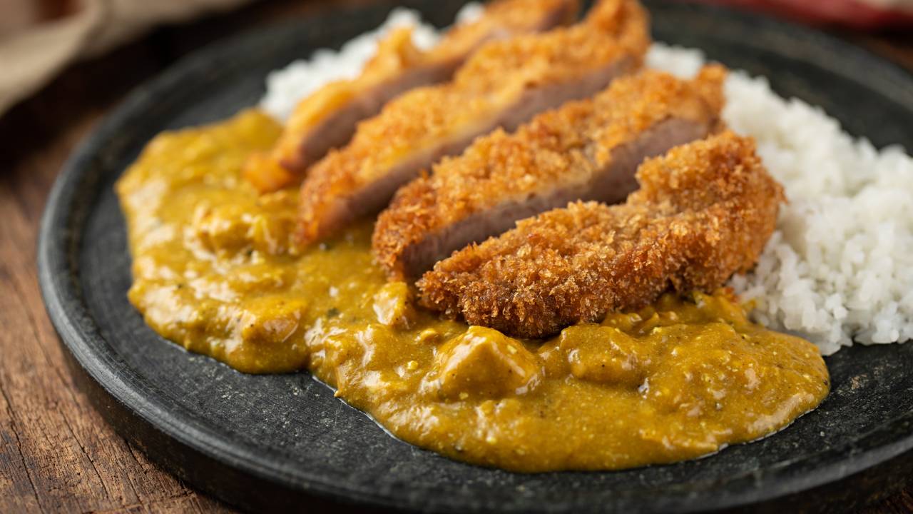 A imagem mostra um lombo suíno à milanesa sobre molho curry