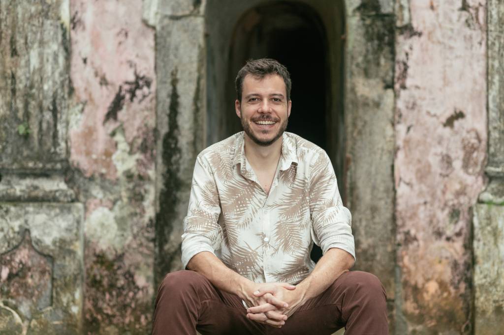 João Cavalcanti sentado na escadinha em frente a uma porta