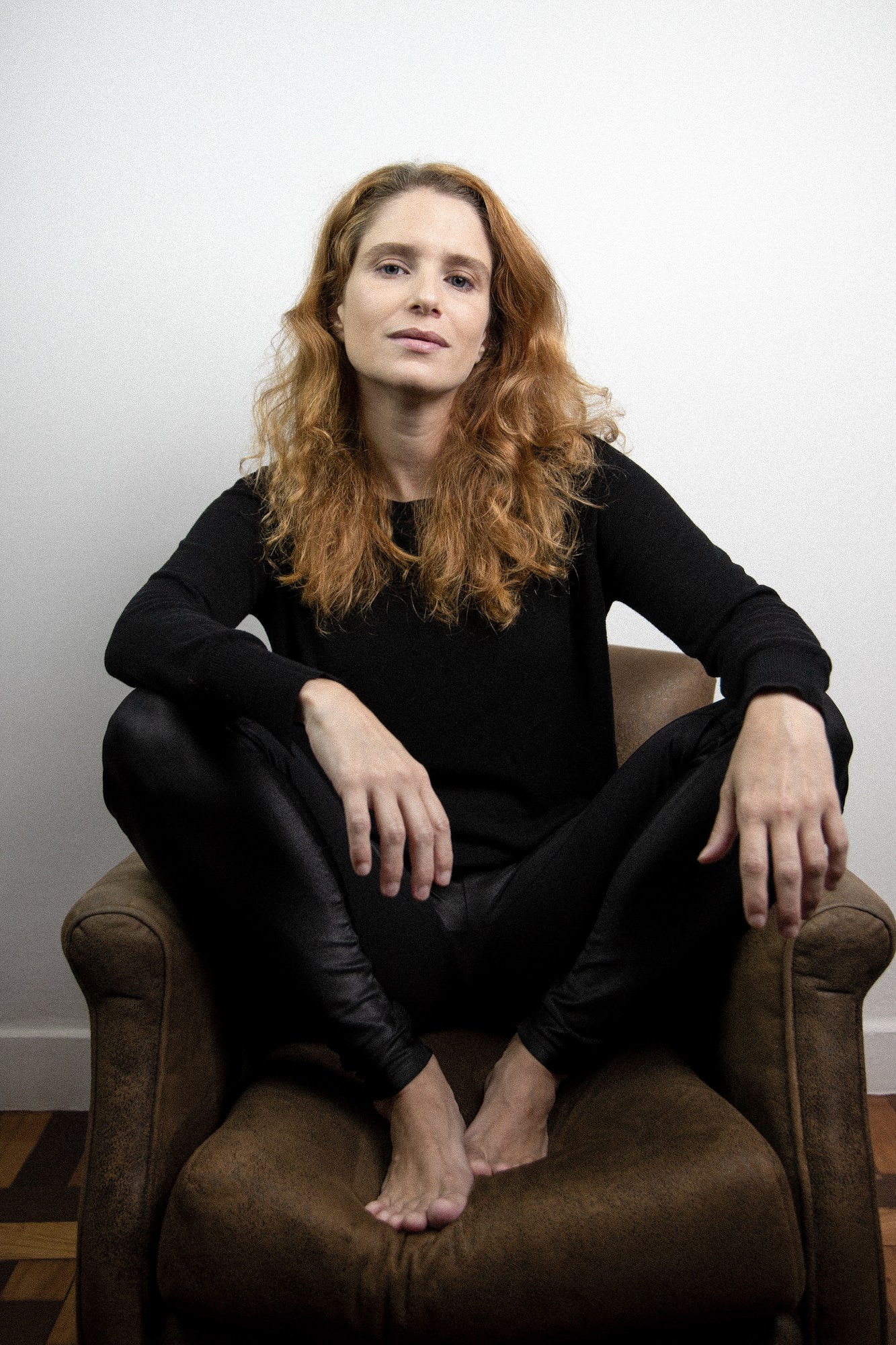 Julia Lund Atriz Julia Lund sentada numa poltrona, com os pés em cima do móvel