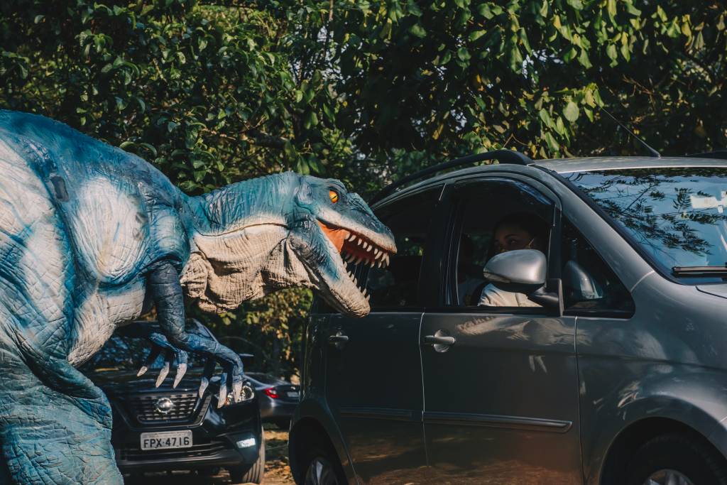 Réplica de tiranossauro rex ao lado de um carro