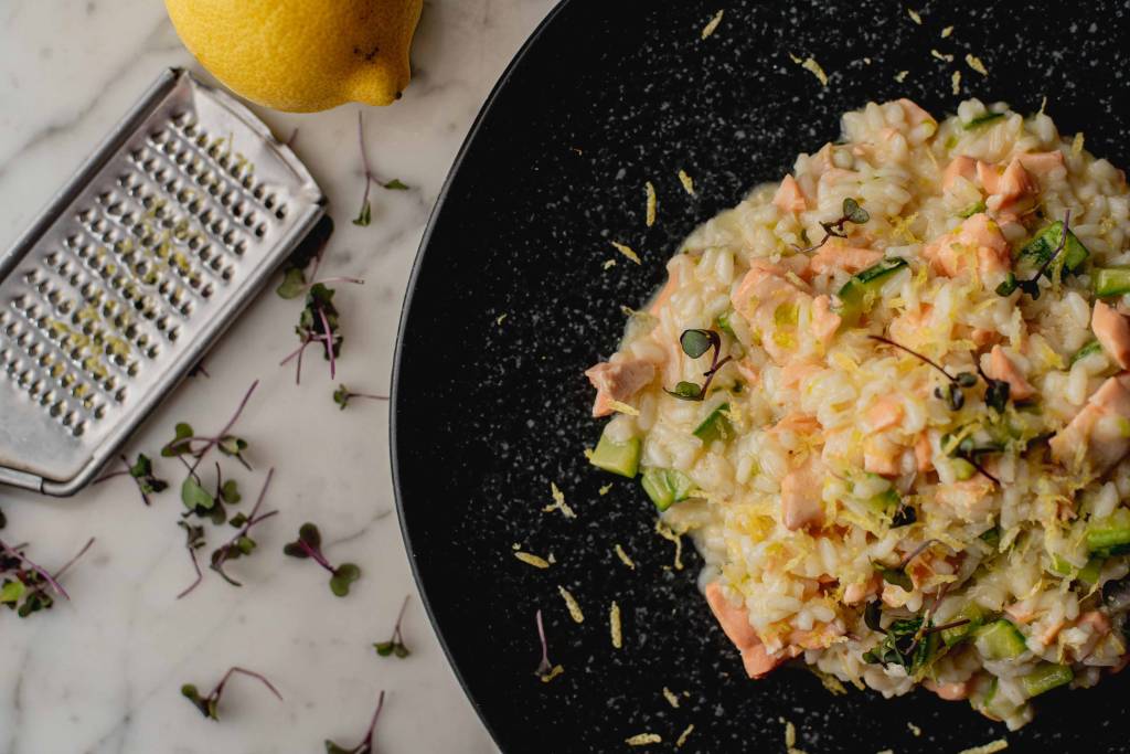 A imagem mostra um prato com risoto de abobrinha e salmão e queijo ralado em volta