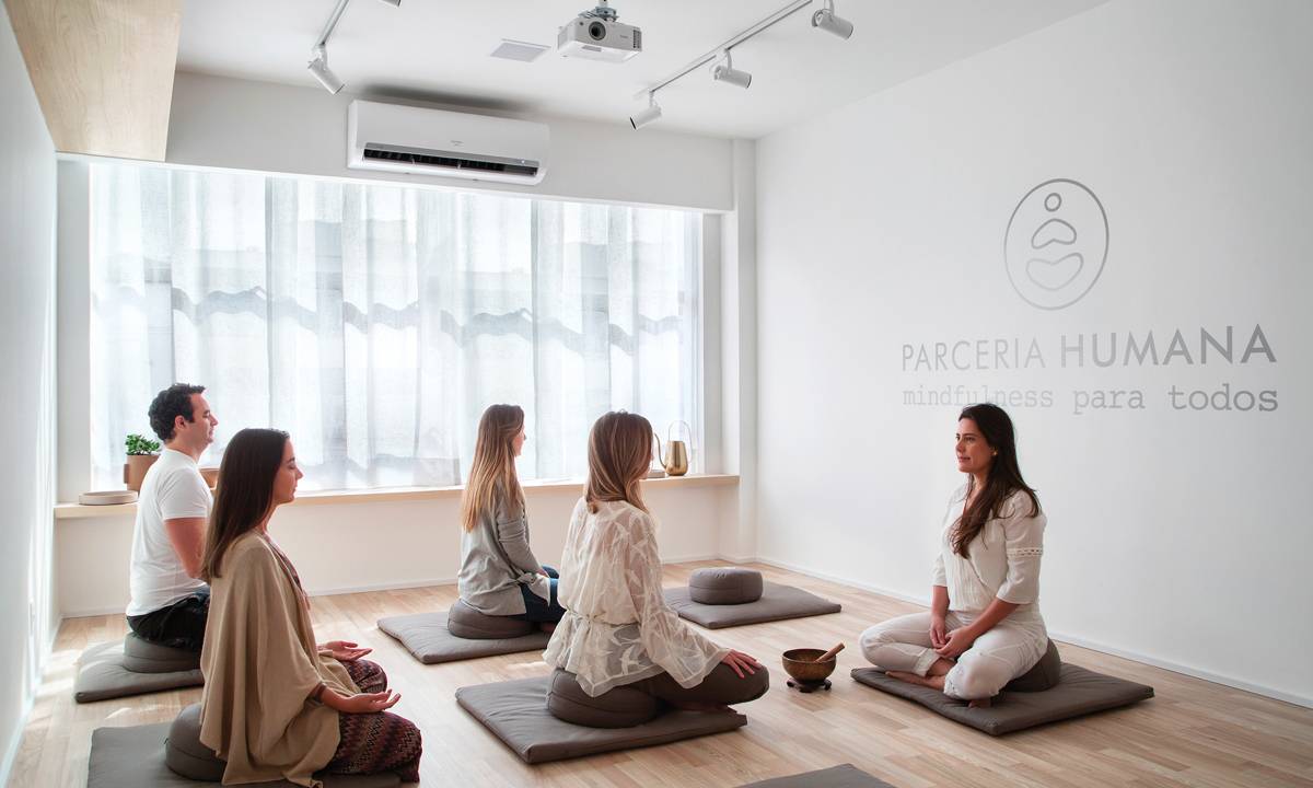 Aula de meditação com professora e três alunas sentada em colchões com as pernas cruzadas