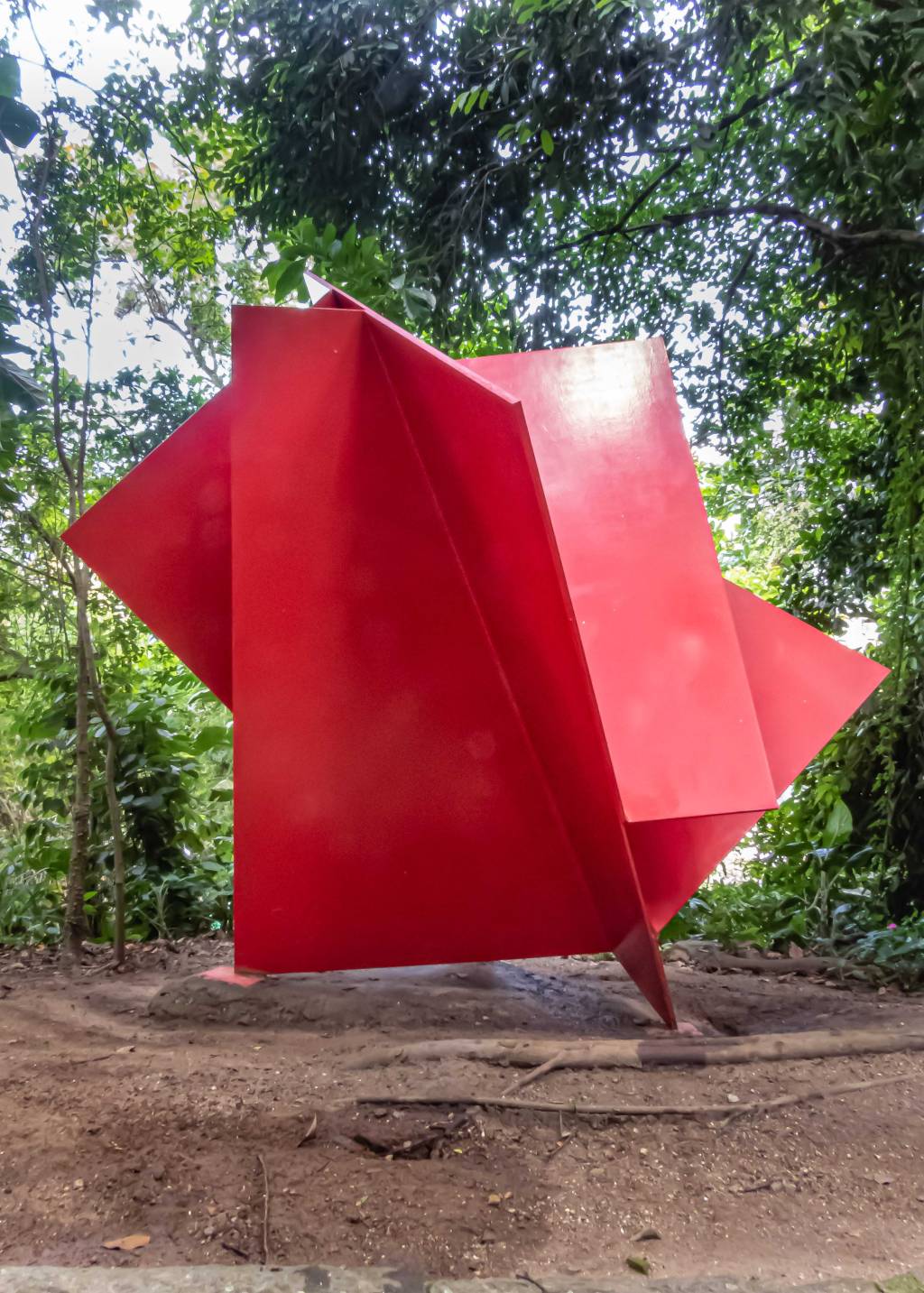 Escultura em formato gigante, com placas vermelhas, num fundo com muitas árvores