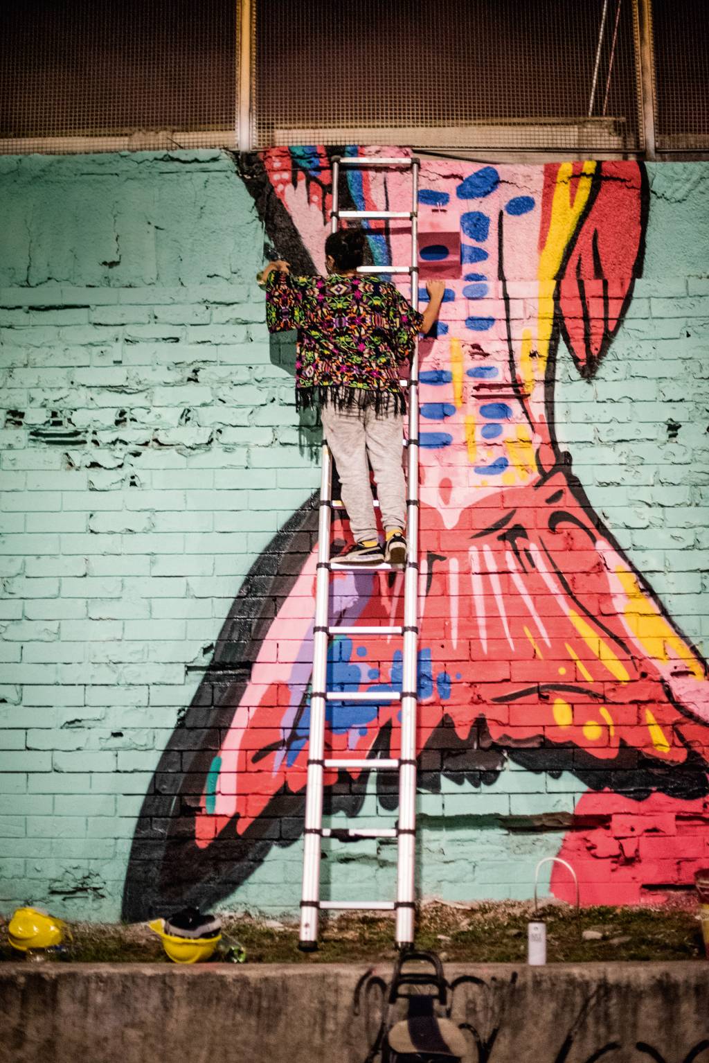 A imagem mostra a grafiteira Dolores Esos numa escada, fazendo arte num muro