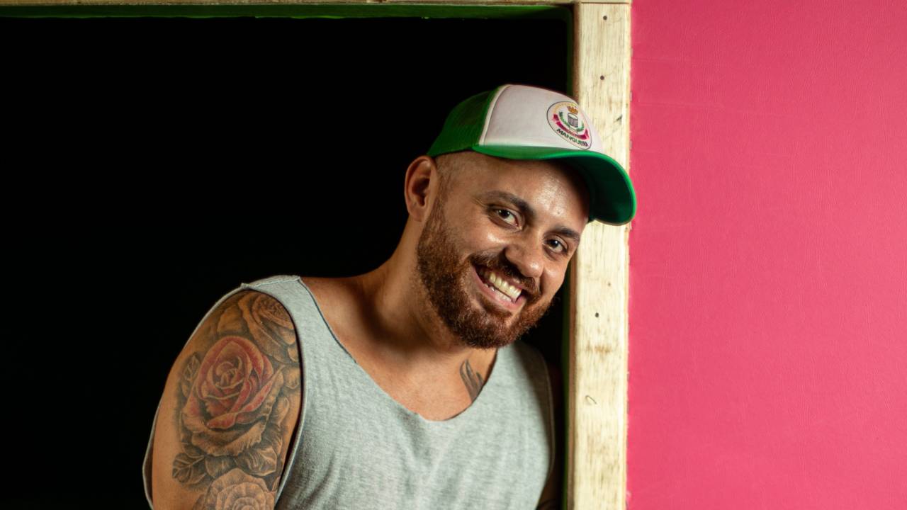 A imagem mostra o carnavalesco Leandro Vieira, da Mangueira, sentado numa janela, com a parede cor de rosa ao fundo