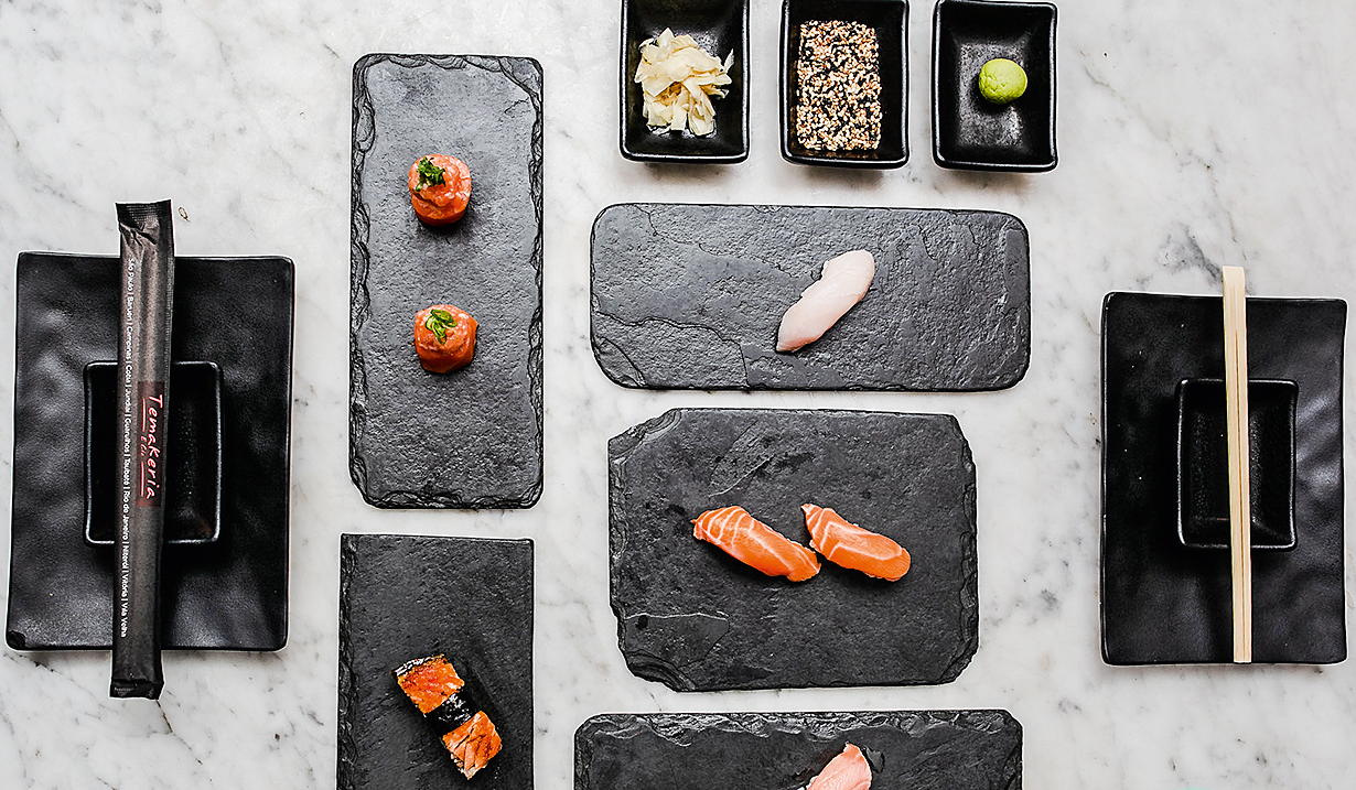 A imagem mostra várias peças de comida japonesa sobre louça em pedra